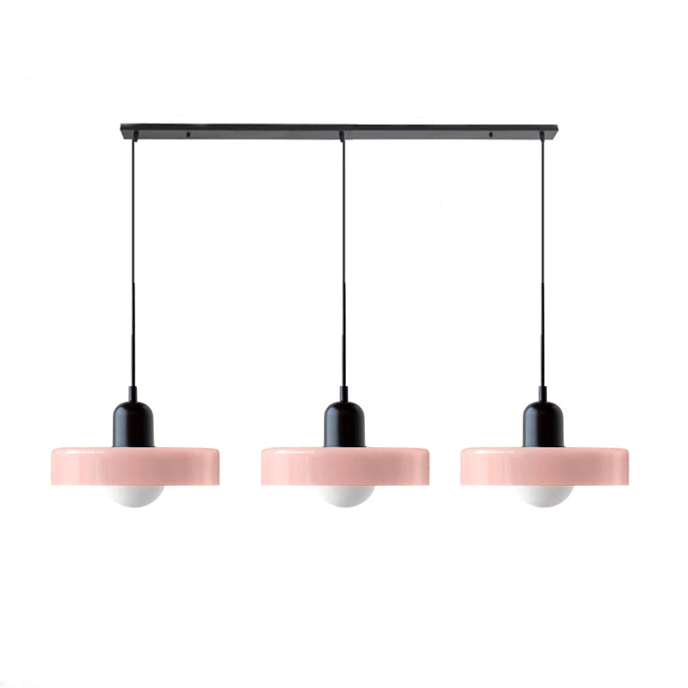 Modern brass pendant lights with adjustable red cable hanging from ceiling above a wooden table in an industrial kitchen setting.