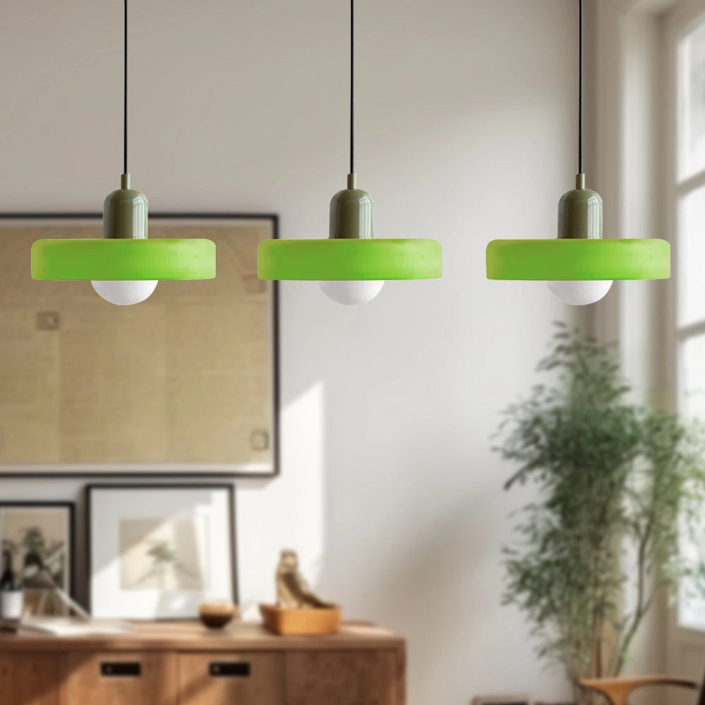 Modern brass pendant lights with three heads, featuring adjustable red cables, matt green finish, and hung in an industrial kitchen setting with wooden shelves and houseplants.