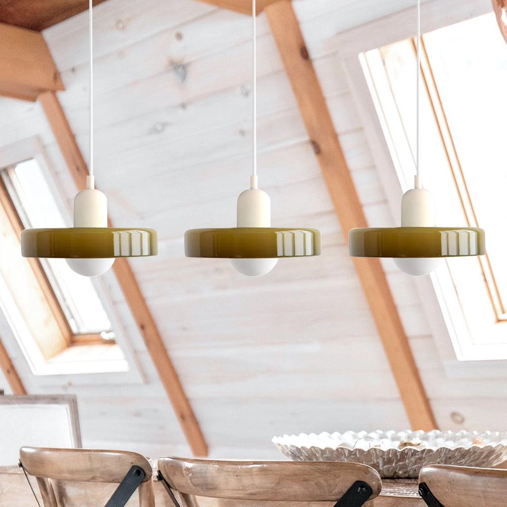 Modern brass pendant lights with three adjustable heads and red cables, featuring green and white shades, hanging in an industrial kitchen with hardwood flooring.