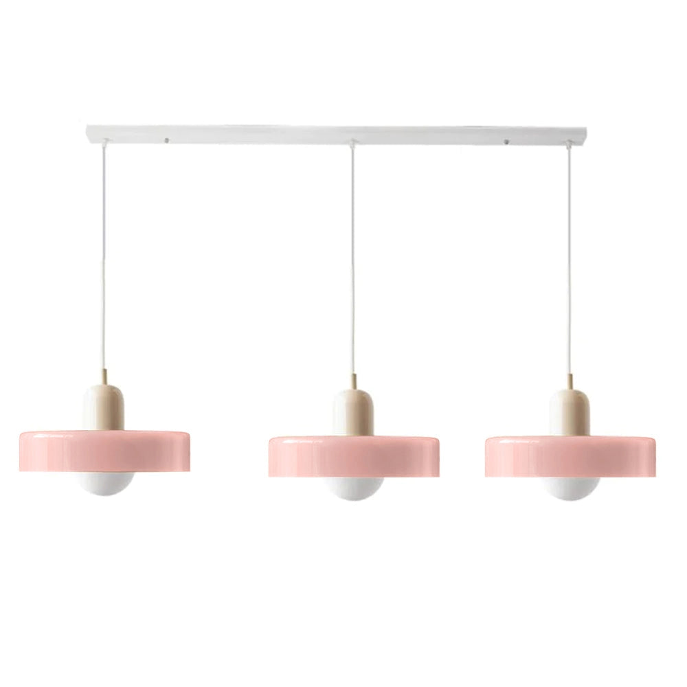 Modern brass pendant light with adjustable red cable hanging above a wooden table in an industrial kitchen setting.