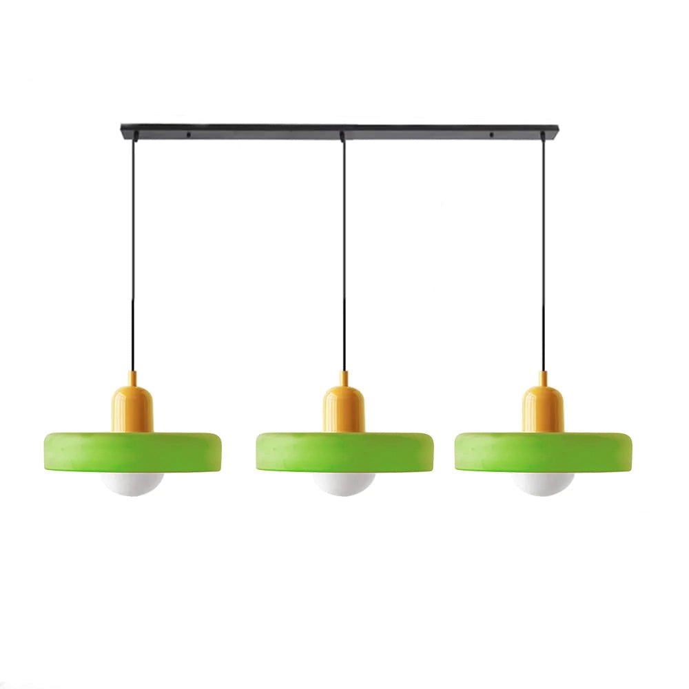 Modern brass pendant lights with red cable hanging over an industrial kitchen island, featuring adjustable height, wooden floors, shelves with home accessories, and green plants.
