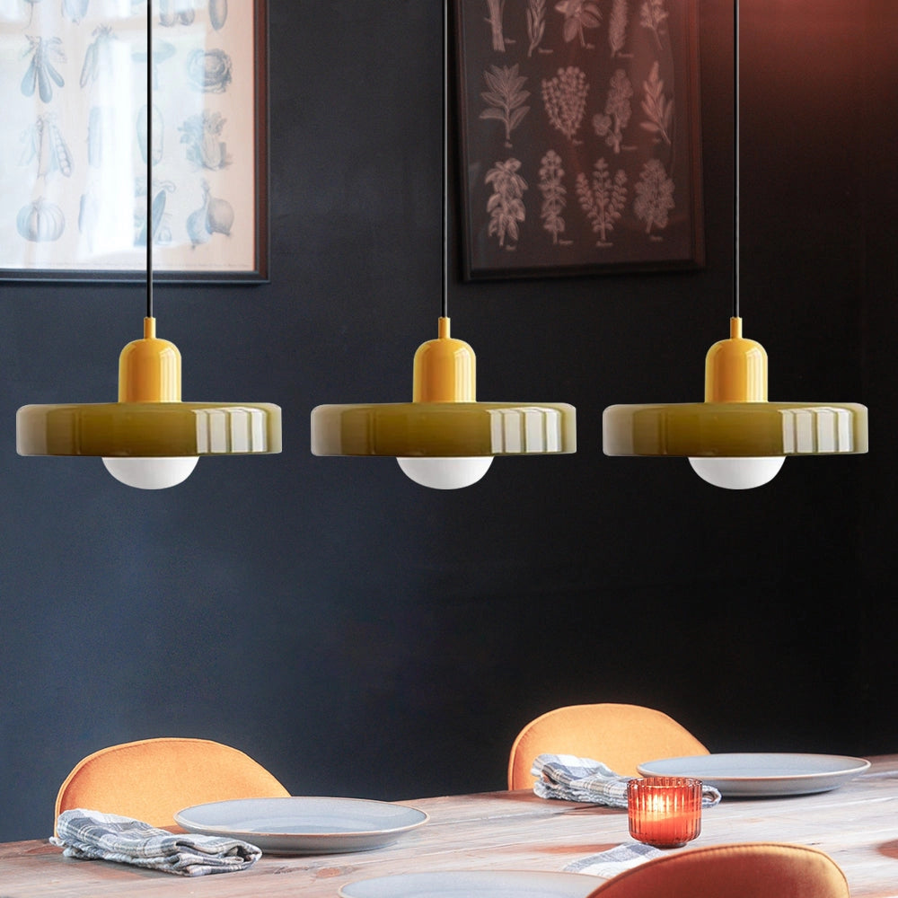 Modern brass pendant lights with a red cable and green-yellow shades, featuring three heads, hanging over a wooden kitchen table with tableware and a candle in an industrial-style kitchen.
