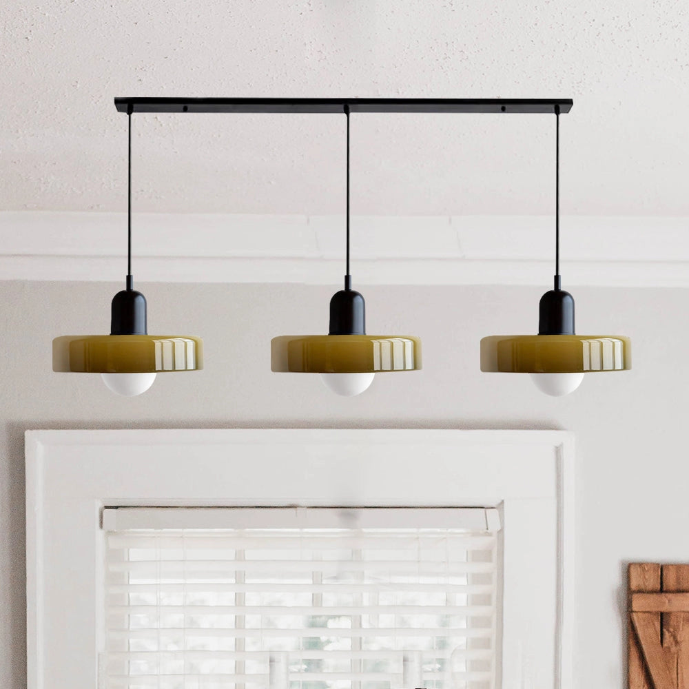 Modern brass pendant lights with three adjustable heads, featuring a green and black design with a red cable, suspended from a ceiling in an industrial kitchen setting.