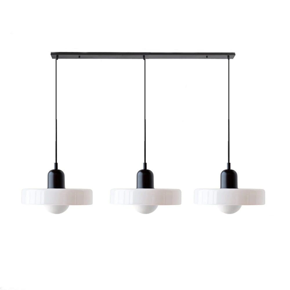 Modern brass pendant light with red cable hanging from ceiling above a kitchen table with shelves in the background.