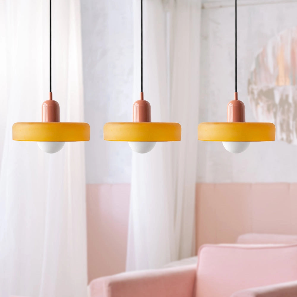 Modern brass pendant lights with three adjustable heads featuring a red cable, hanging from the ceiling against an orange and pink backdrop.
