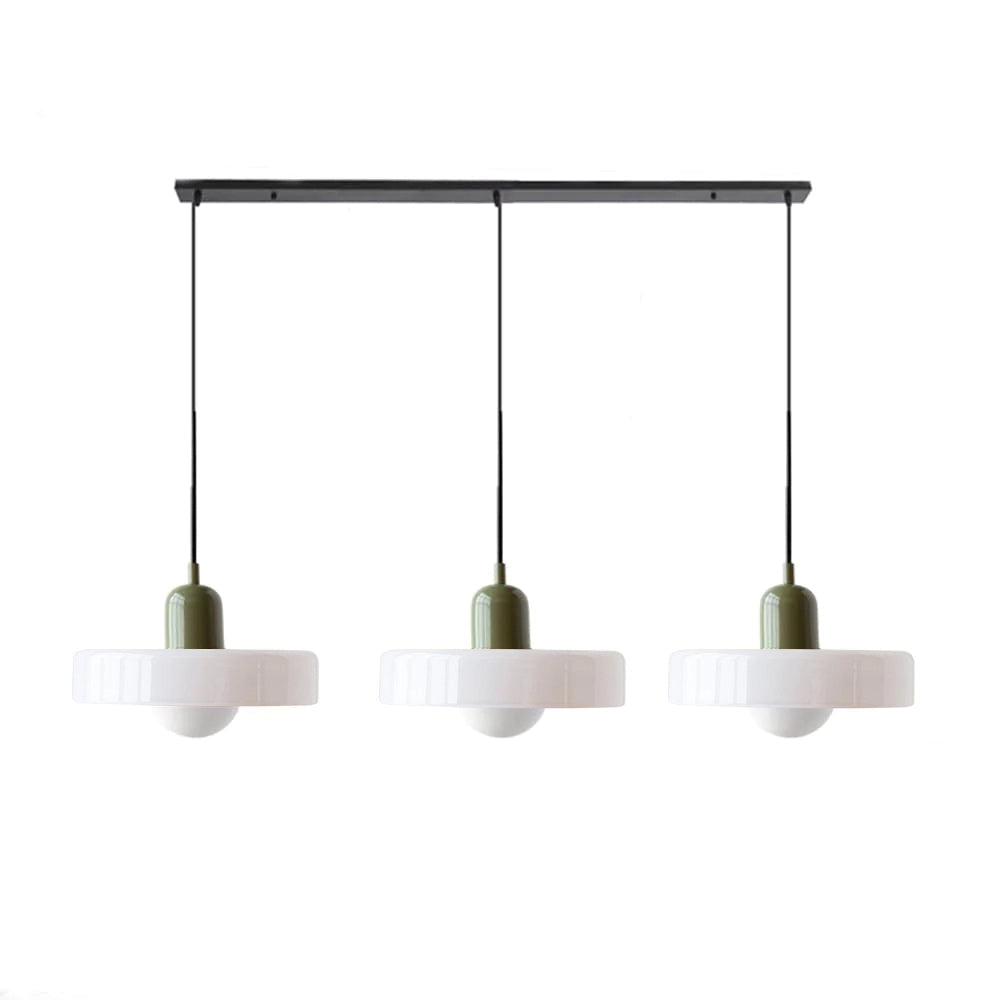 Modern brass pendant light with adjustable red cable hanging from the ceiling in an industrial-style kitchen, with shelves and plants in the background.