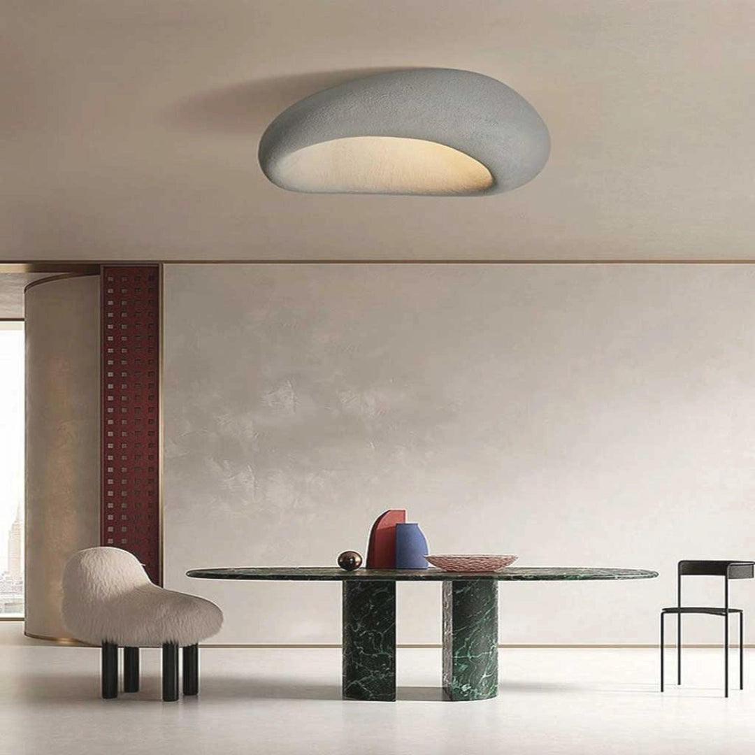 A modern ceiling lamp providing warm ambient lighting, suspended above a minimalist interior setting featuring wooden furniture and flooring.