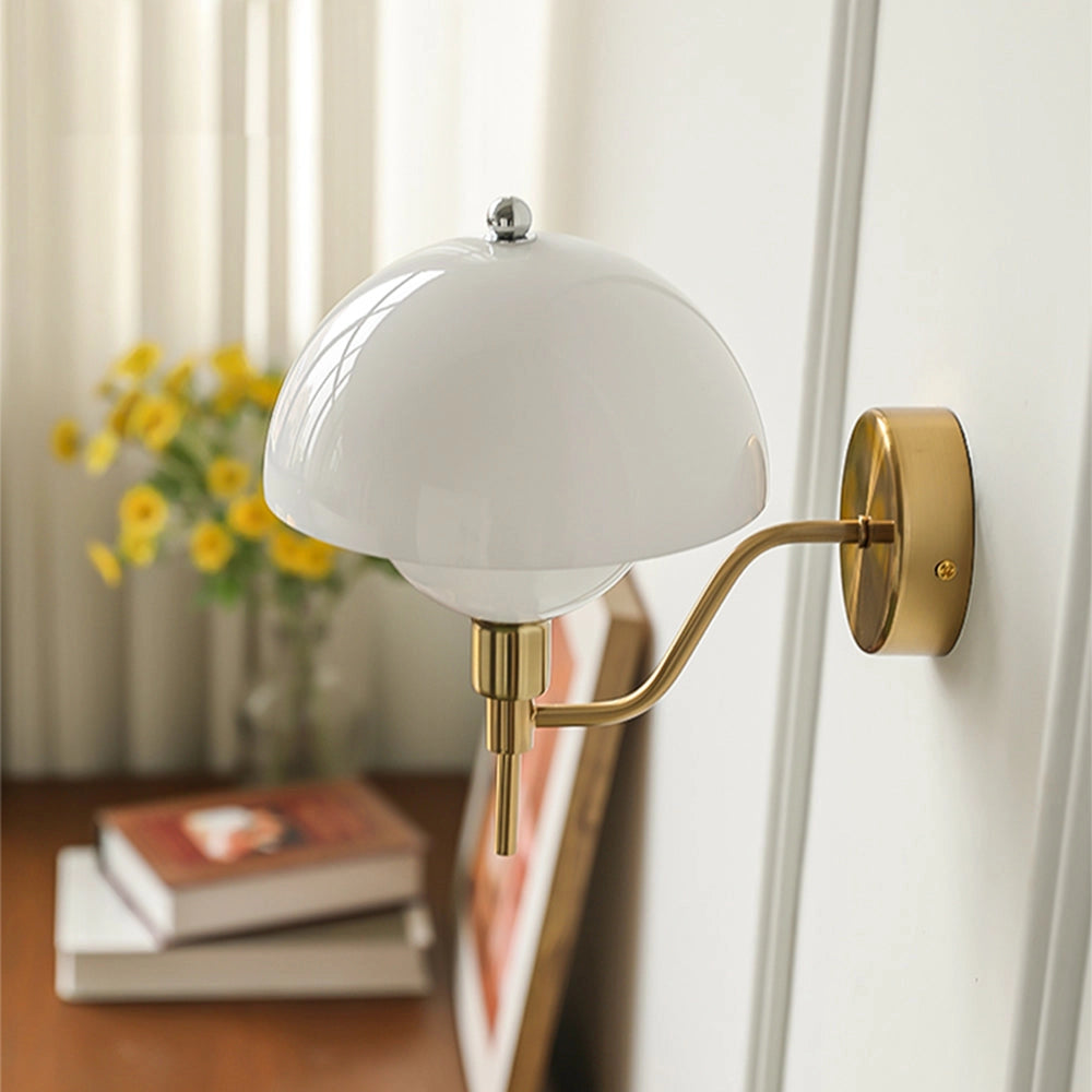Modern chrome wall sconce with a minimalist design, featuring an adjustable arm, mounted on a wooden wall. The lamp is positioned above a table adorned with a small potted plant and a flower, enhancing the bedroom's decor.