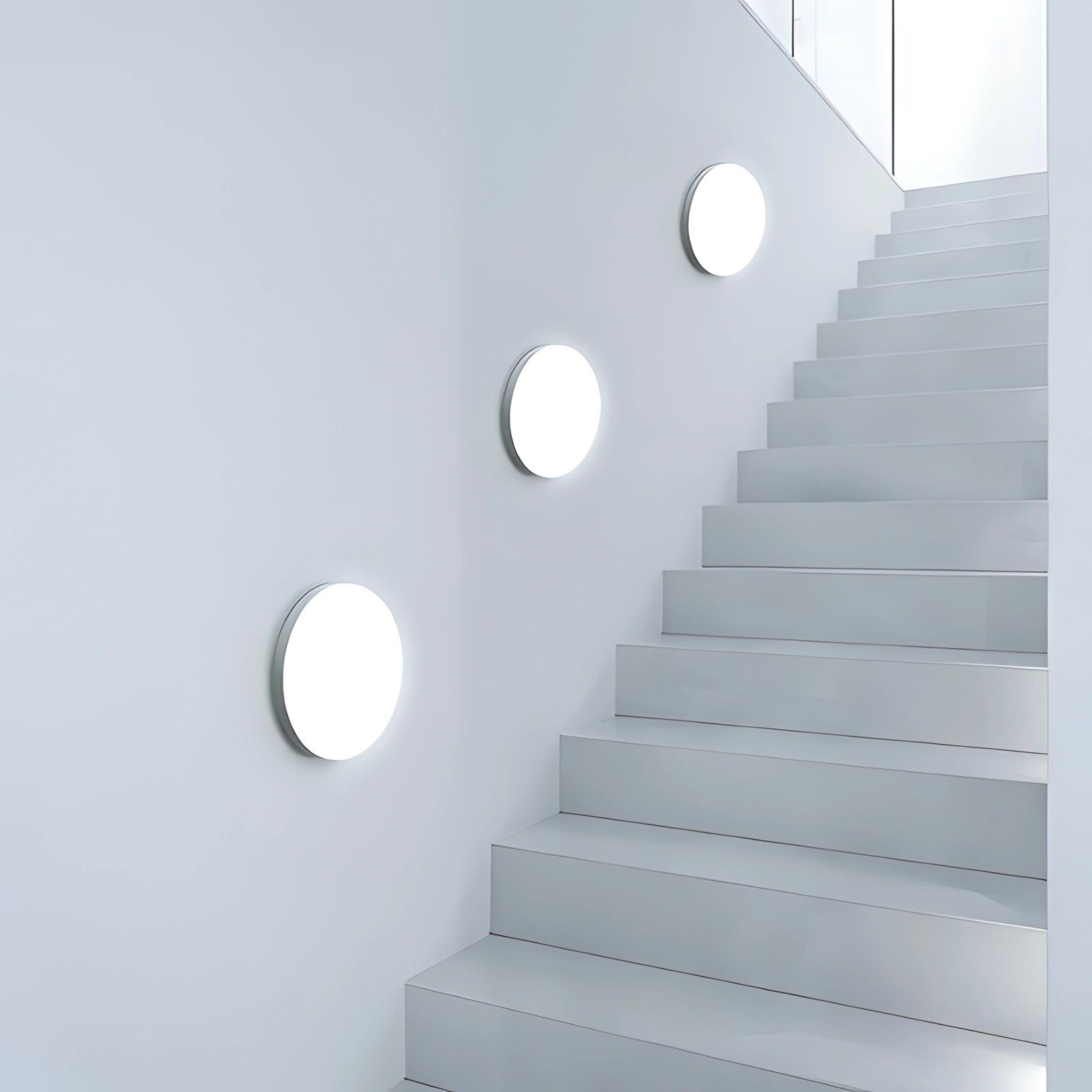 Modern circular wall lights installed on a staircase wall, featuring a minimalist design with a futuristic aesthetic, surrounded by wooden and plaster elements.