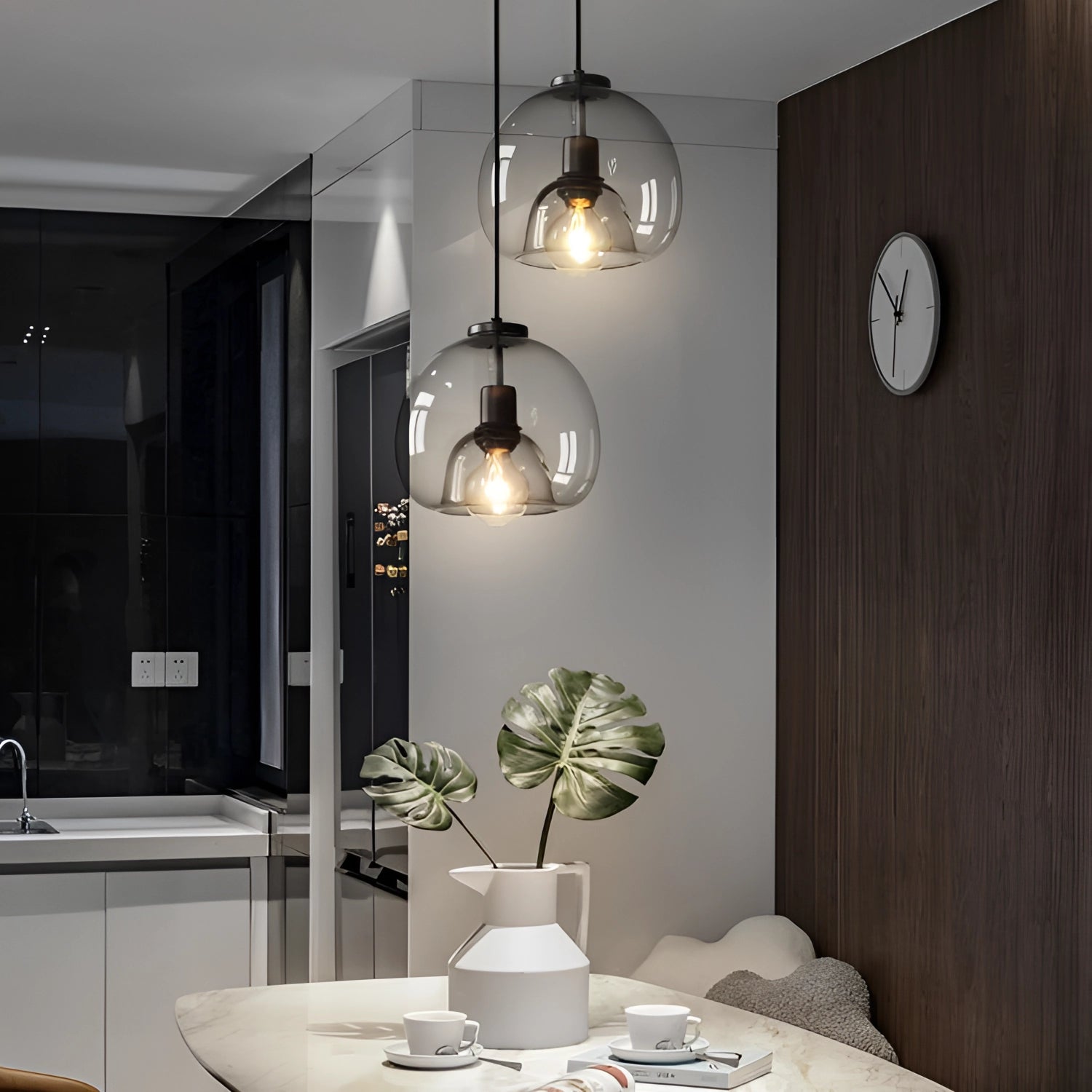 Modern clear glass pendant lights hanging above a stylishly set table with white tableware and a small plant, showcasing a contemporary interior design.