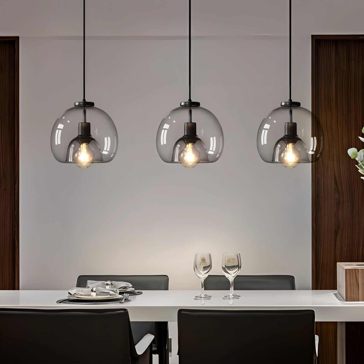 Modern clear glass pendant lights with stylish globe design hanging from the ceiling, illuminating a wooden table in a well-designed interior space.