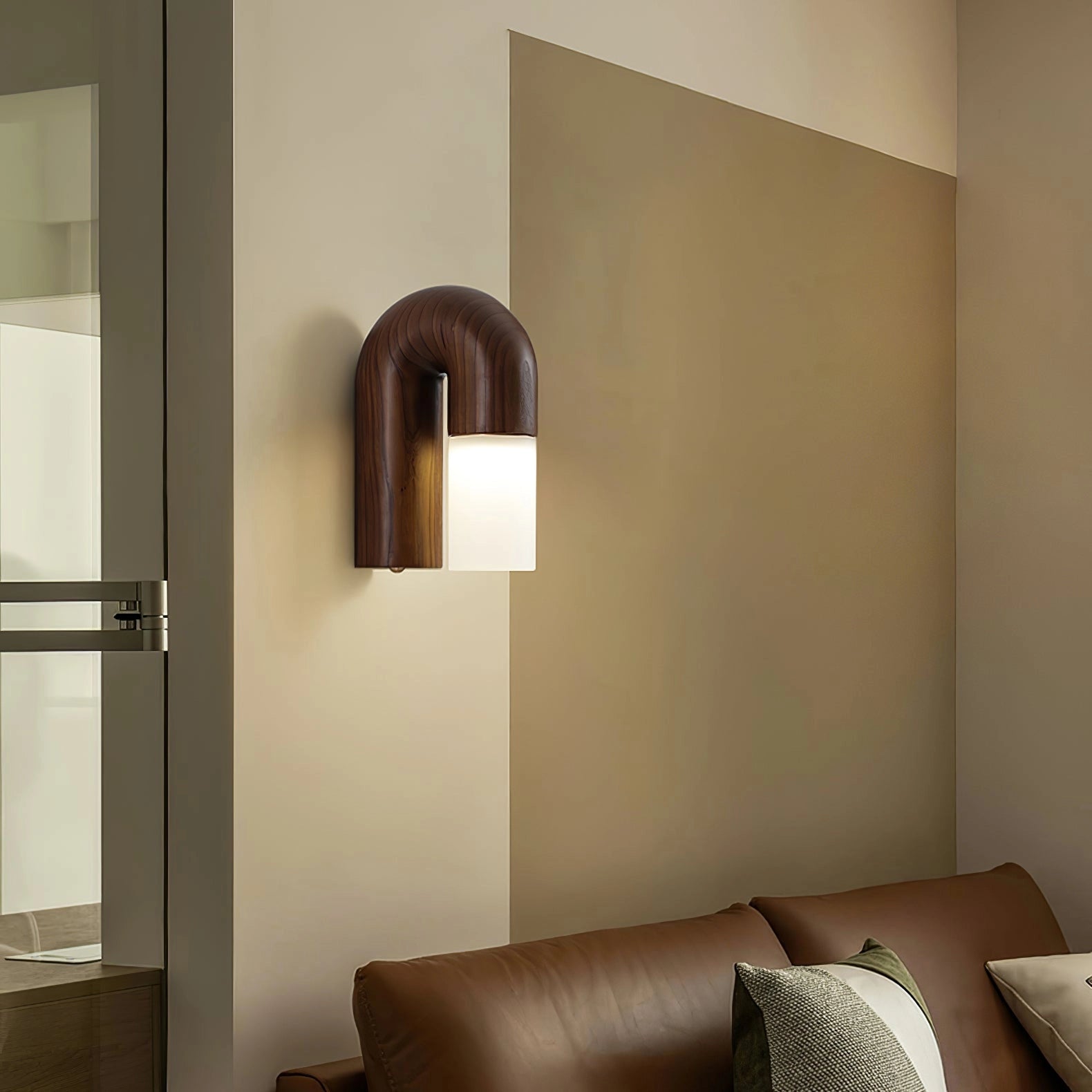 Modern curved wooden wall sconce with LED lighting, featuring a minimalist arch design; mounted on a wall with visible hardwood flooring and adjacent furniture elements.