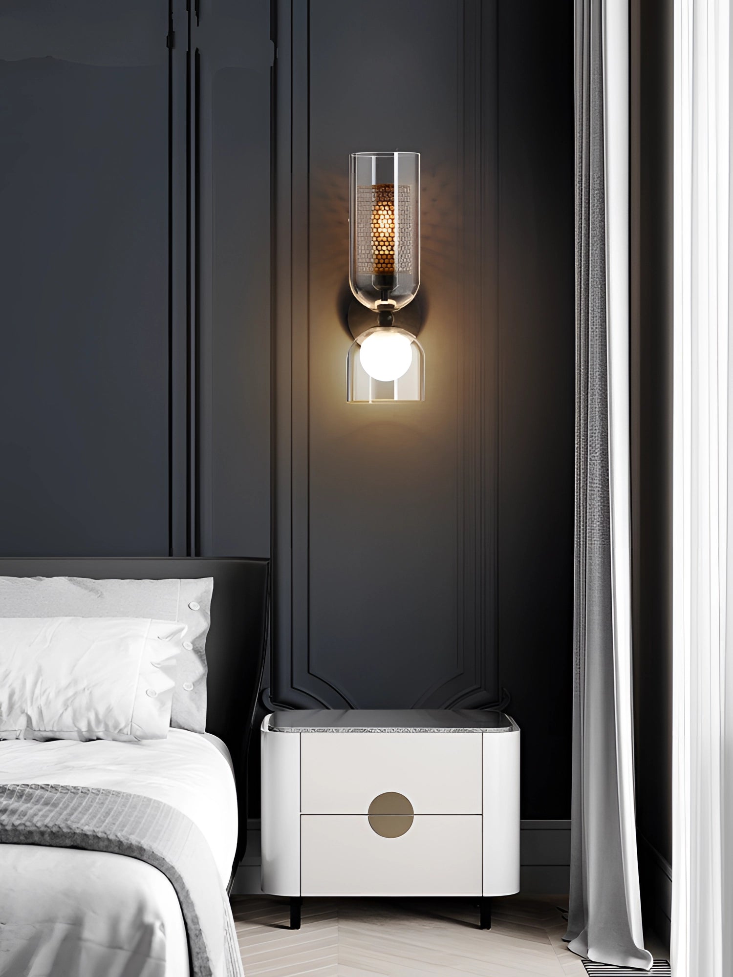 Modern cylindrical glass wall sconce with a bronze mesh shade mounted on a wall, illuminating a stylish interior space with contemporary design elements.