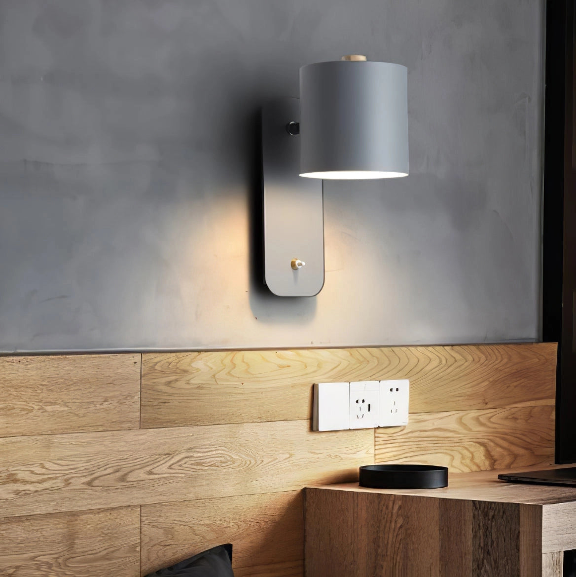 
A modern cylindrical LED wall lamp mounted on a minimalist metal sconce, positioned on a wooden wall in a stylish living room setting.