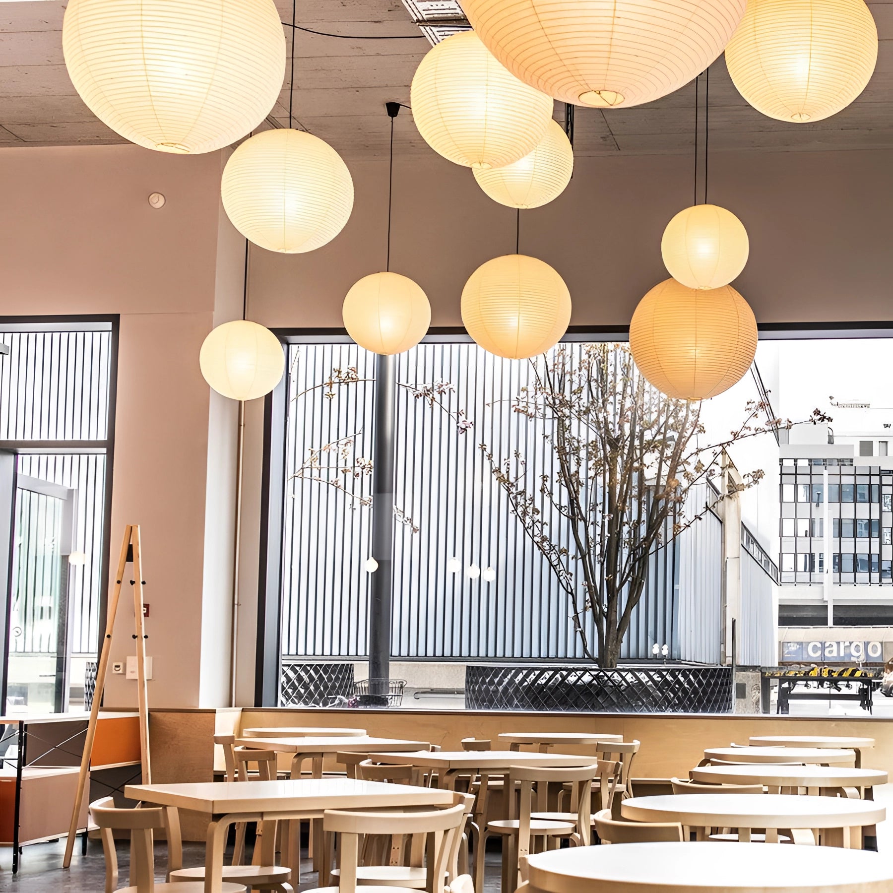 Modern designer paper lantern pendant hanging in a stylish interior setting, offering minimalist ambient lighting alongside a window and wooden table, complementing the contemporary decor and architecture.