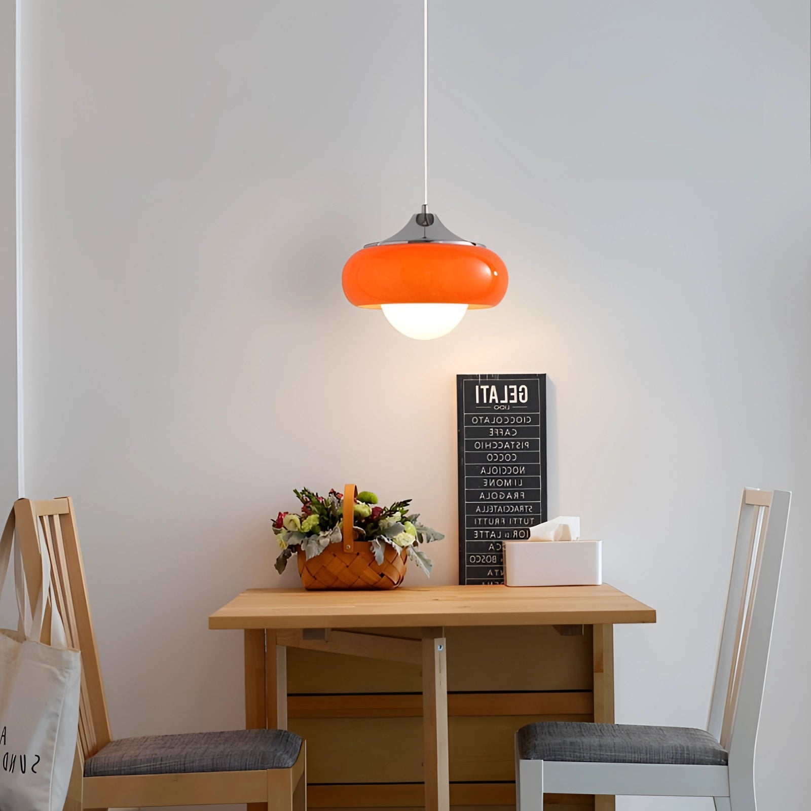 Modern dual color pendant lamps in Scandinavian mid-century style hanging above a wooden table adorned with a potted houseplant, surrounded by shelving and a chair, creating a cozy and stylish ambiance.