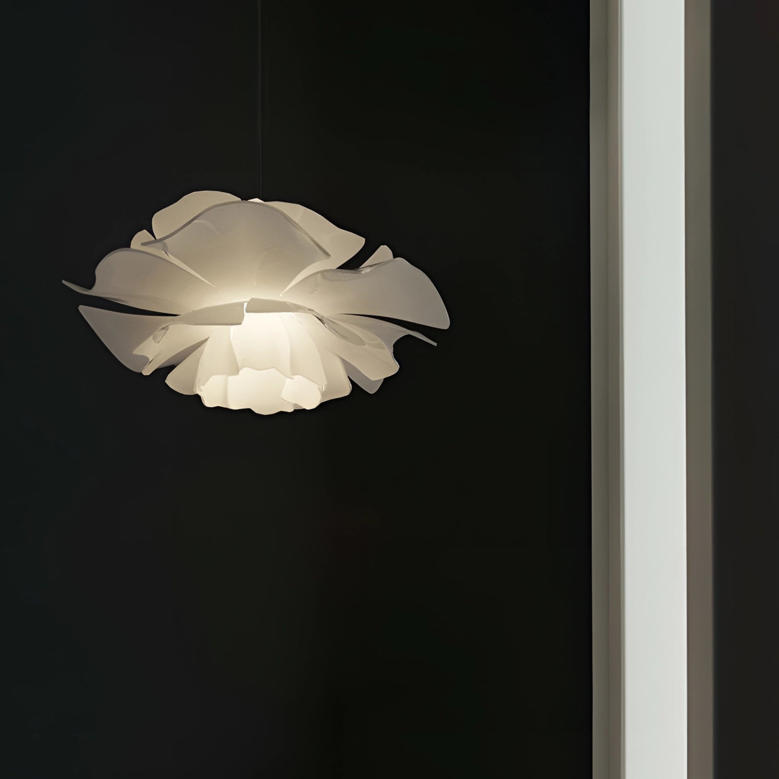 Modern flower-shaped pendant light with petal design and glass elements hanging from the ceiling, illuminating the dark room.