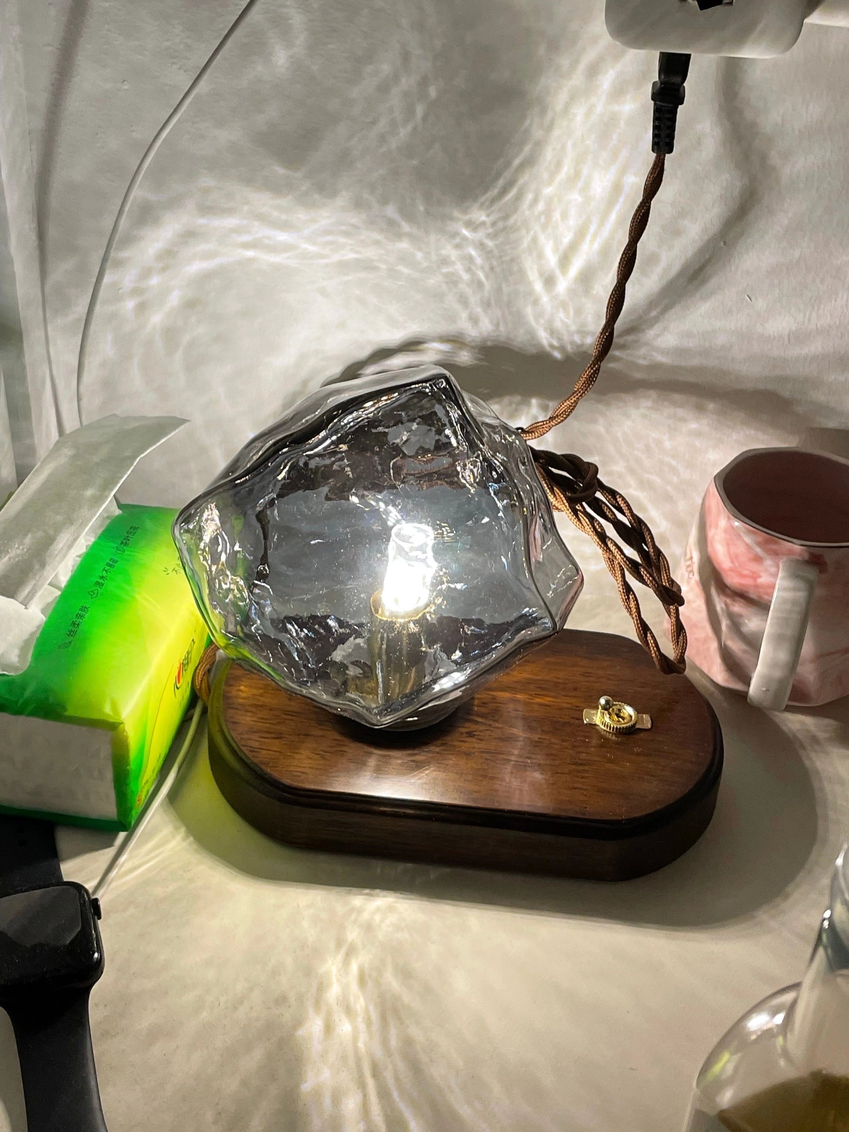 Modern geometric glass desk lamp with wooden base on a table.