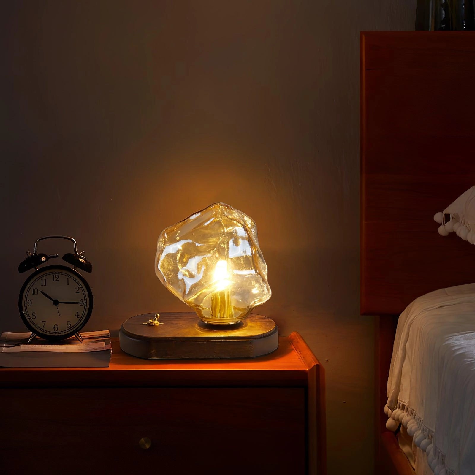 Modern geometric glass desk lamp with amber light, wooden base, and artistic design placed on a table.