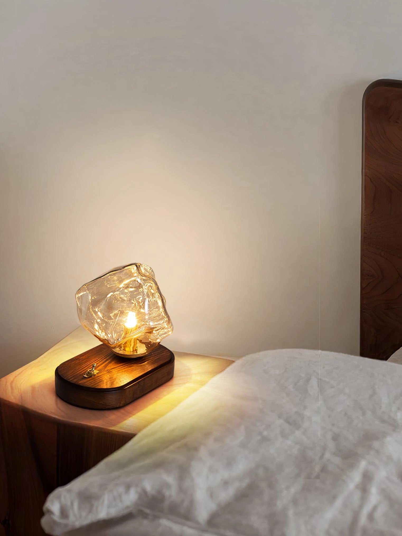 Modern geometric glass desk lamp with amber glow and wooden base on a table.