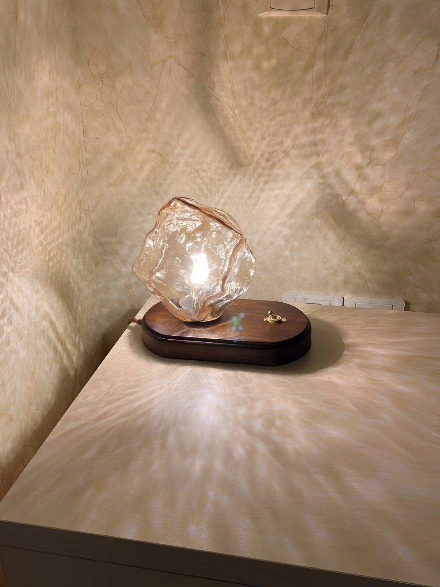 Modern geometric glass desk lamp with wooden base on hardwood flooring, featuring artistic design elements and natural materials.