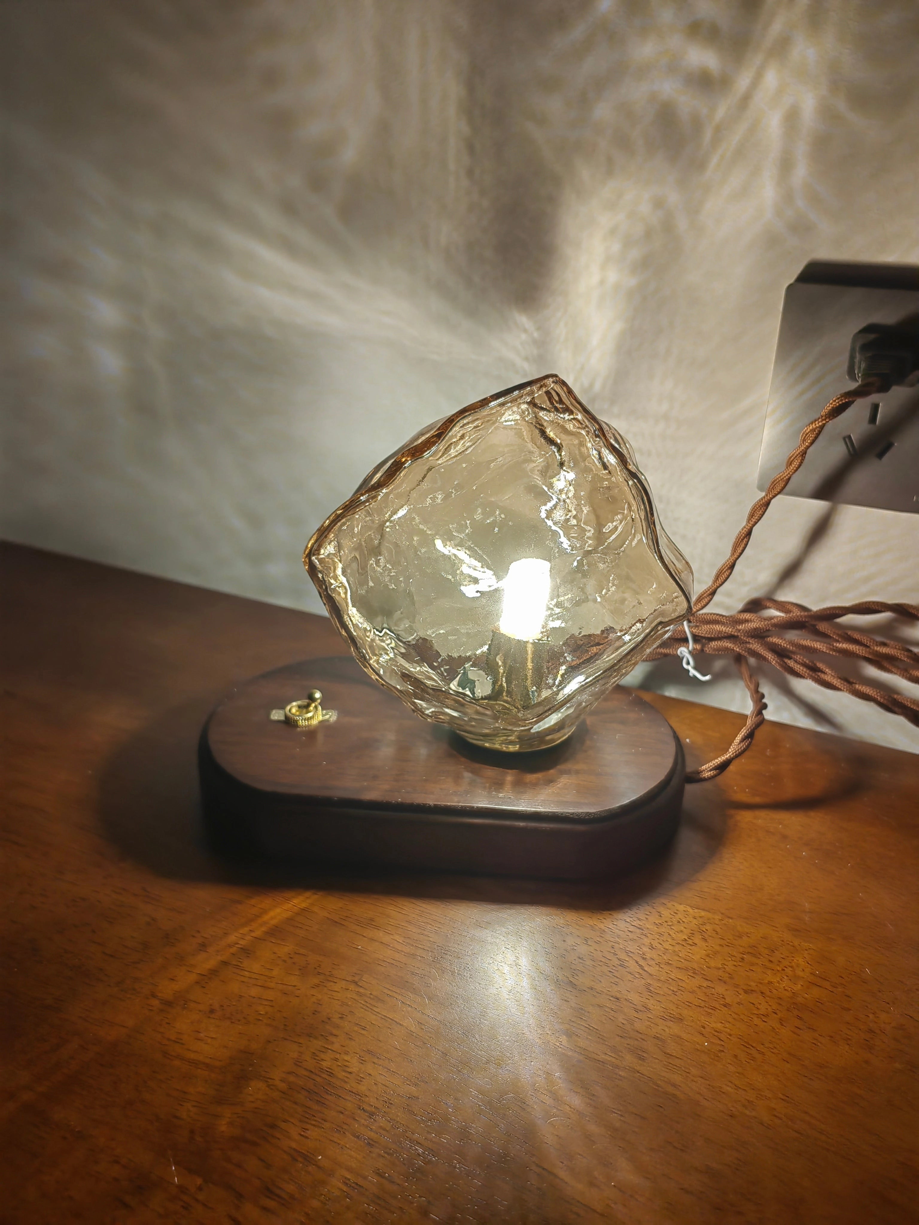 Modern geometric glass desk lamp with artistic light and wooden base, featuring a warm amber glow.