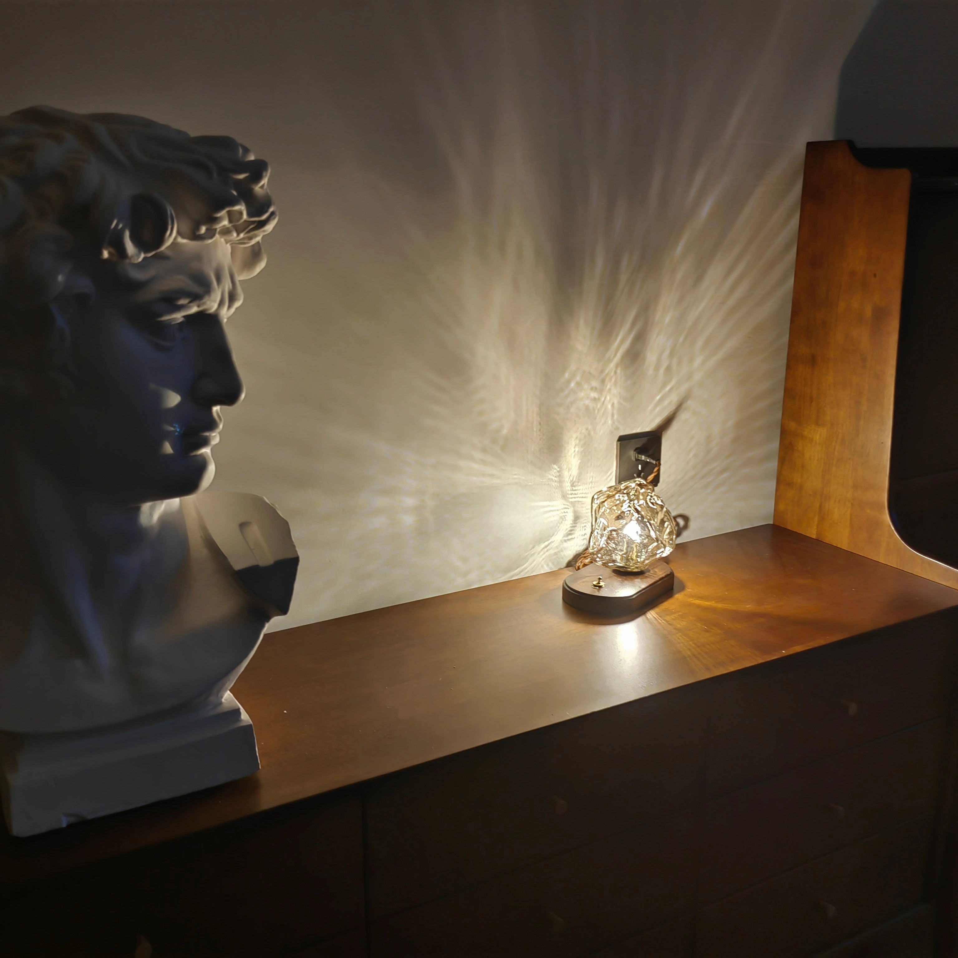 Modern geometric glass desk lamp with wooden base on a table, illuminating a room with artistic light.