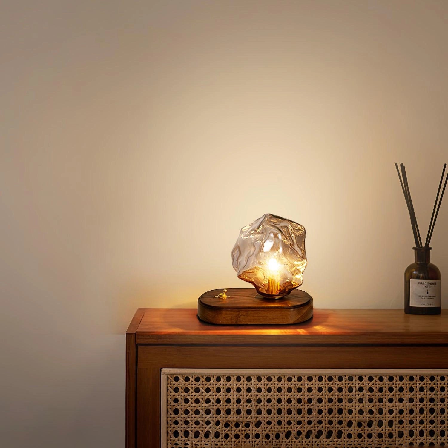 Modern Geometric Glass Desk Lamp with Wooden Base, featuring an amber-tinted glass shade, placed on a table next to a clock, illuminating the space with warm lighting.
