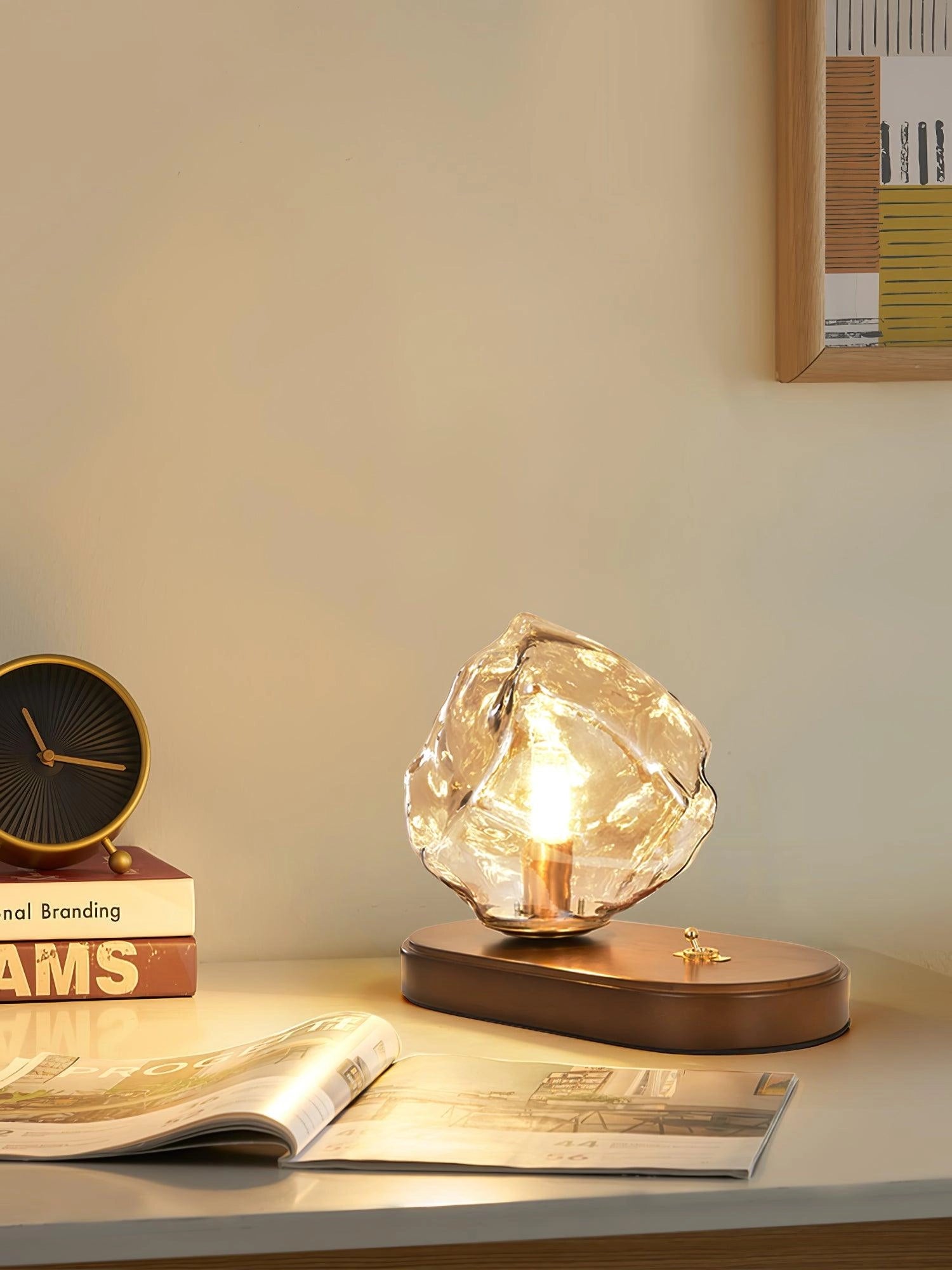 Modern geometric glass desk lamp with an amber glass shade, wooden base, and metal accents in a still life setting.