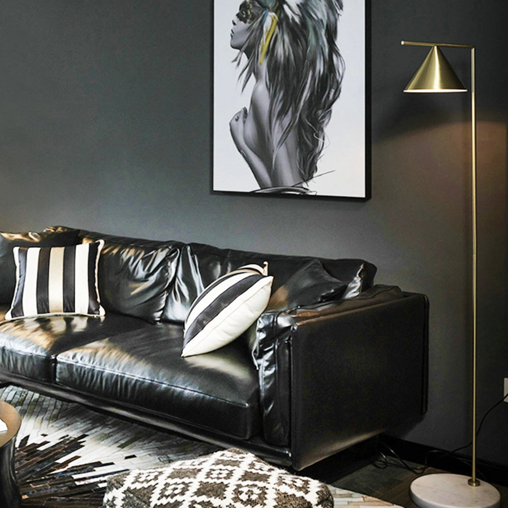 Modern geometric gold floor lamp with a black stand, emitting warm white light, positioned in a stylish interior setting with a grey studio couch.