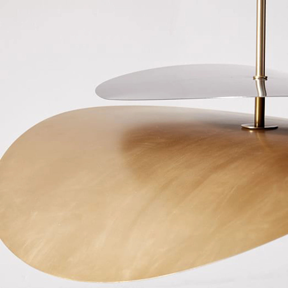 Modern geometric pendant light in gold and grey, hanging above a wooden table with beige chairs on a wooden floor.