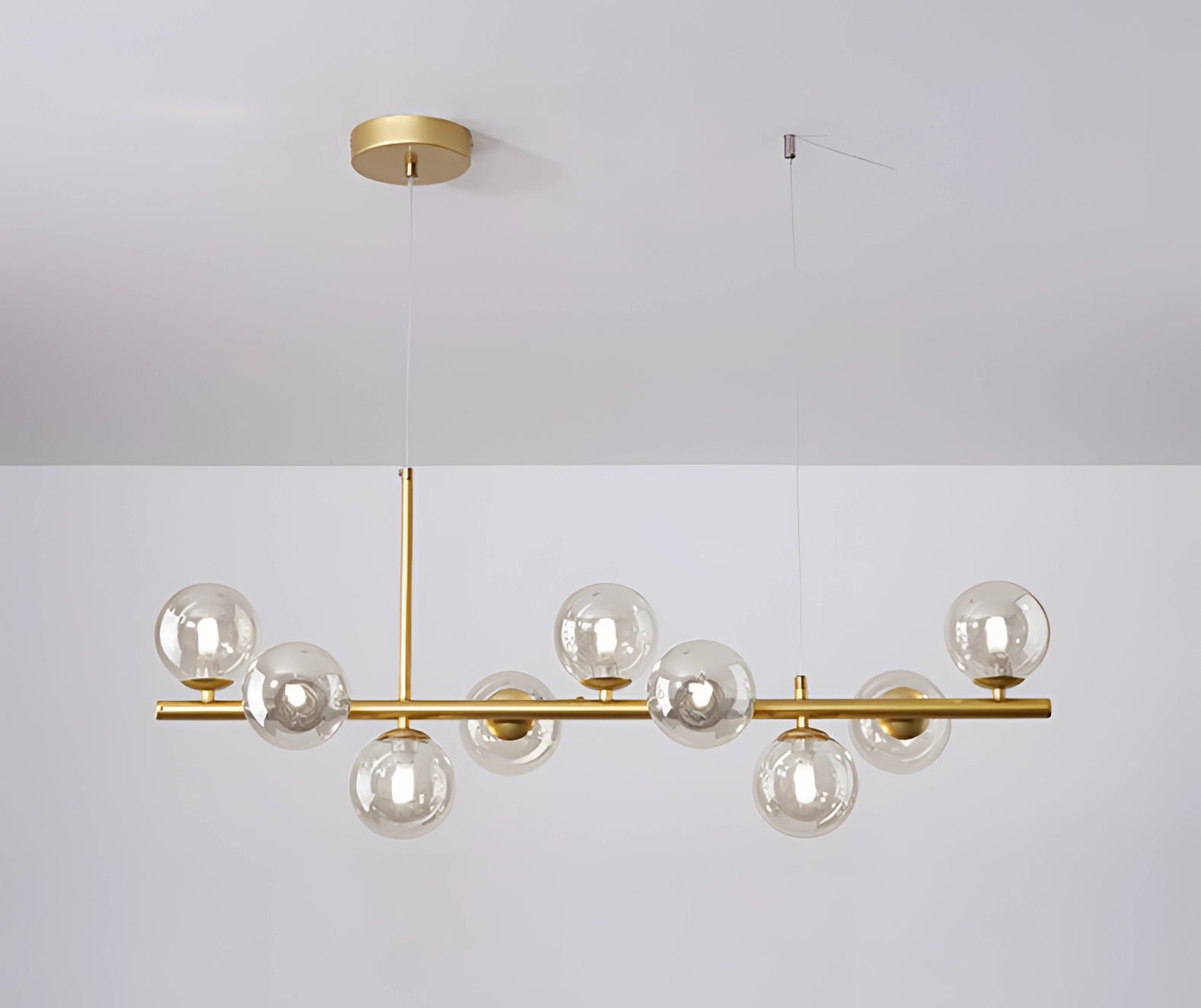 Modern gold and clear glass globe chandelier with adjustable bronze pendant light, featuring a sleek rectangular base and circular glass shades, elegantly hanging from the ceiling.