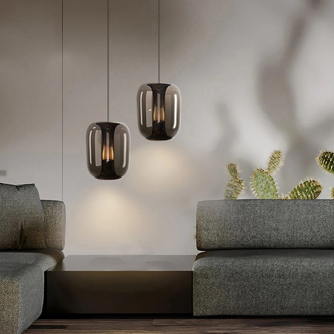 Modern glass LED pendant light fixture with a minimalist design, hanging in a stylish bedroom setting. The image features a rectangular glass lamp illuminating the room, which includes wooden shelving, a potted plant, and wall art enhancing the contemporary interior design.