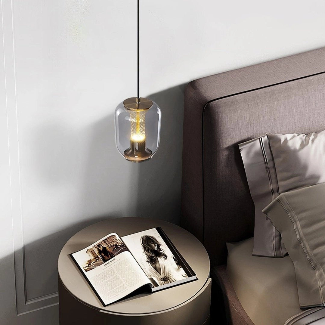 Modern glass LED pendant light fixture with a minimalist design, featuring a sleek silver finish and rectangular shape, suspended over a comfortable setting with chairs.