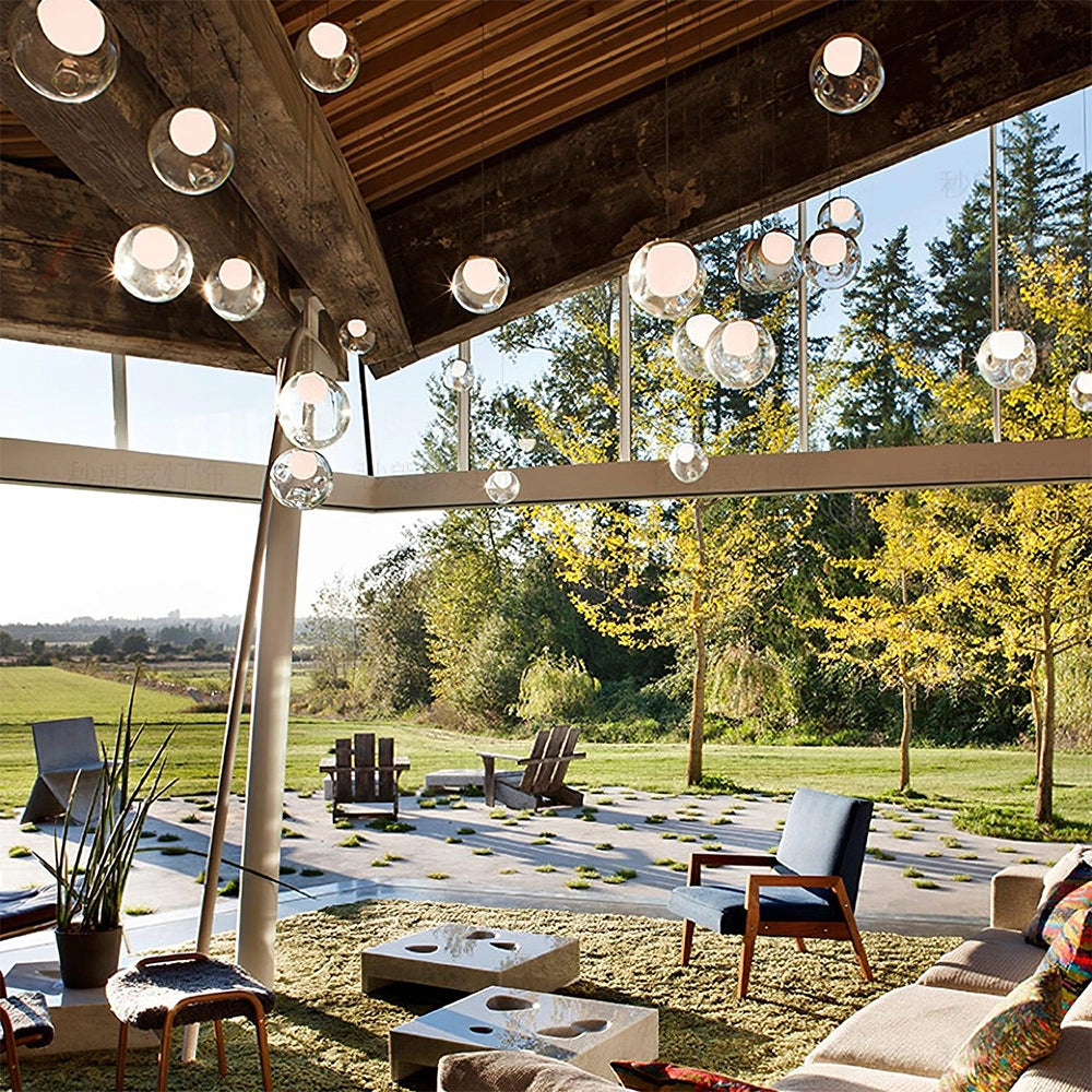 Modern globe pendant chandelier with adjustable LED lights hanging from the ceiling in a stylishly designed interior space, featuring contemporary furniture and decorative plants.