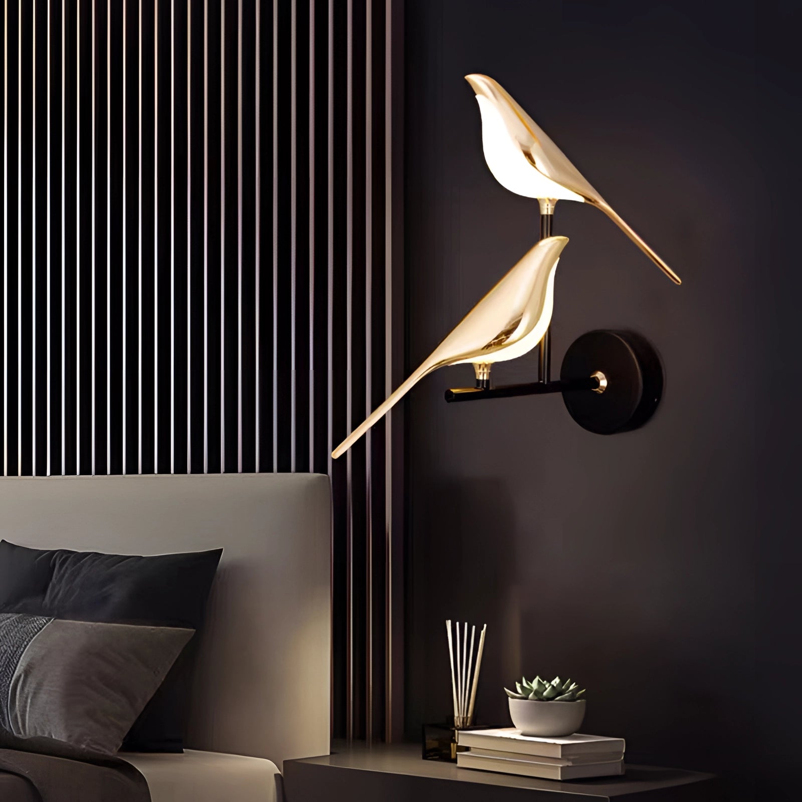 Modern gold bird wall light fixture with a luxurious avian design, mounted on a wall above a black couch and wooden table, illuminating the space with a warm yellow glow.