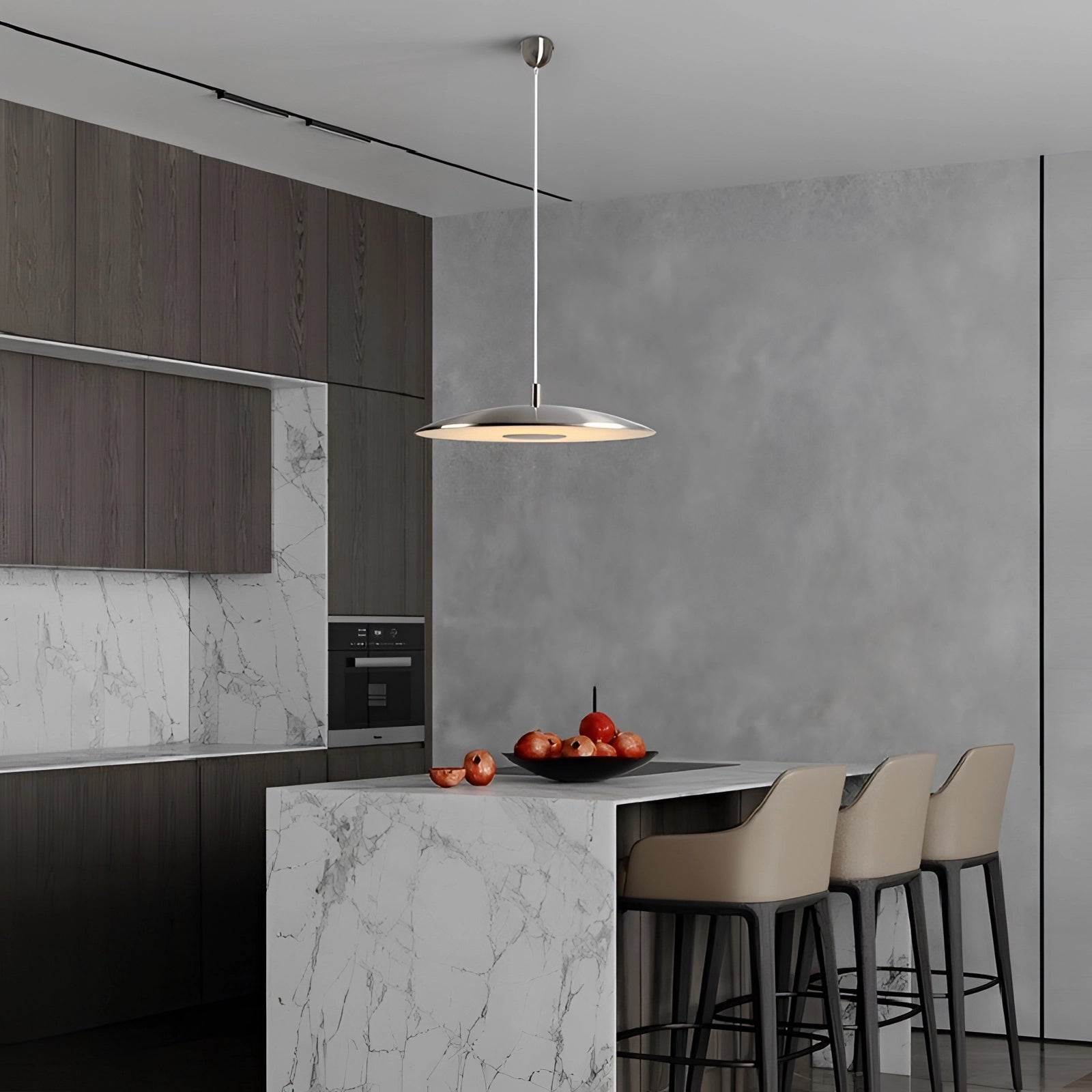 Modern gold-brushed pendant light hanging above a sleek kitchen countertop with grey cabinetry and wooden shelving in a stylish interior design setting.