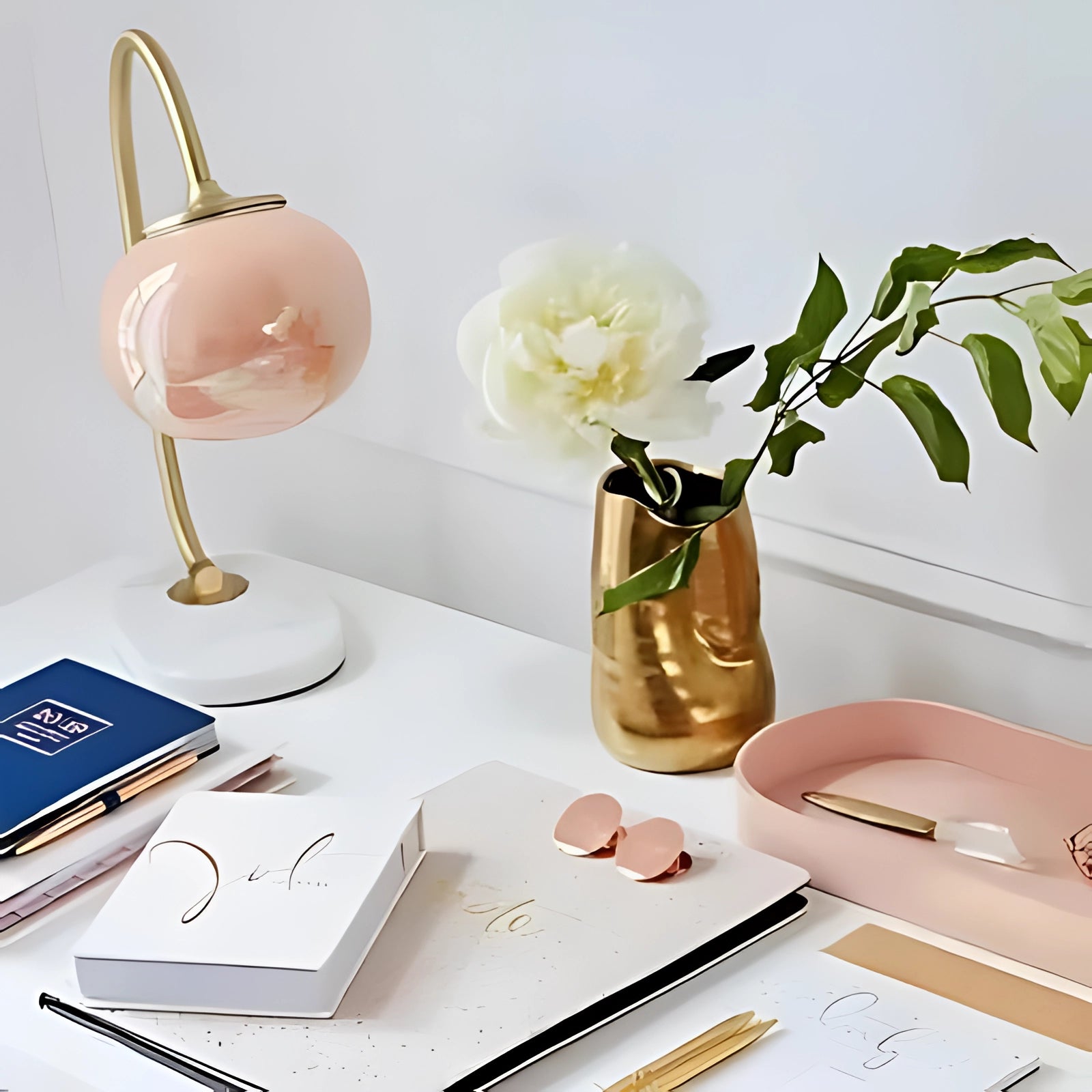 A modern gold finish table lamp with a minimalist curved design, featuring soft lighting. The lamp is styled beside a flowerpot containing a vibrant houseplant, enhancing the aesthetic appeal of the setting. The combination of the gold lamp and greenery creates a warm and inviting atmosphere.