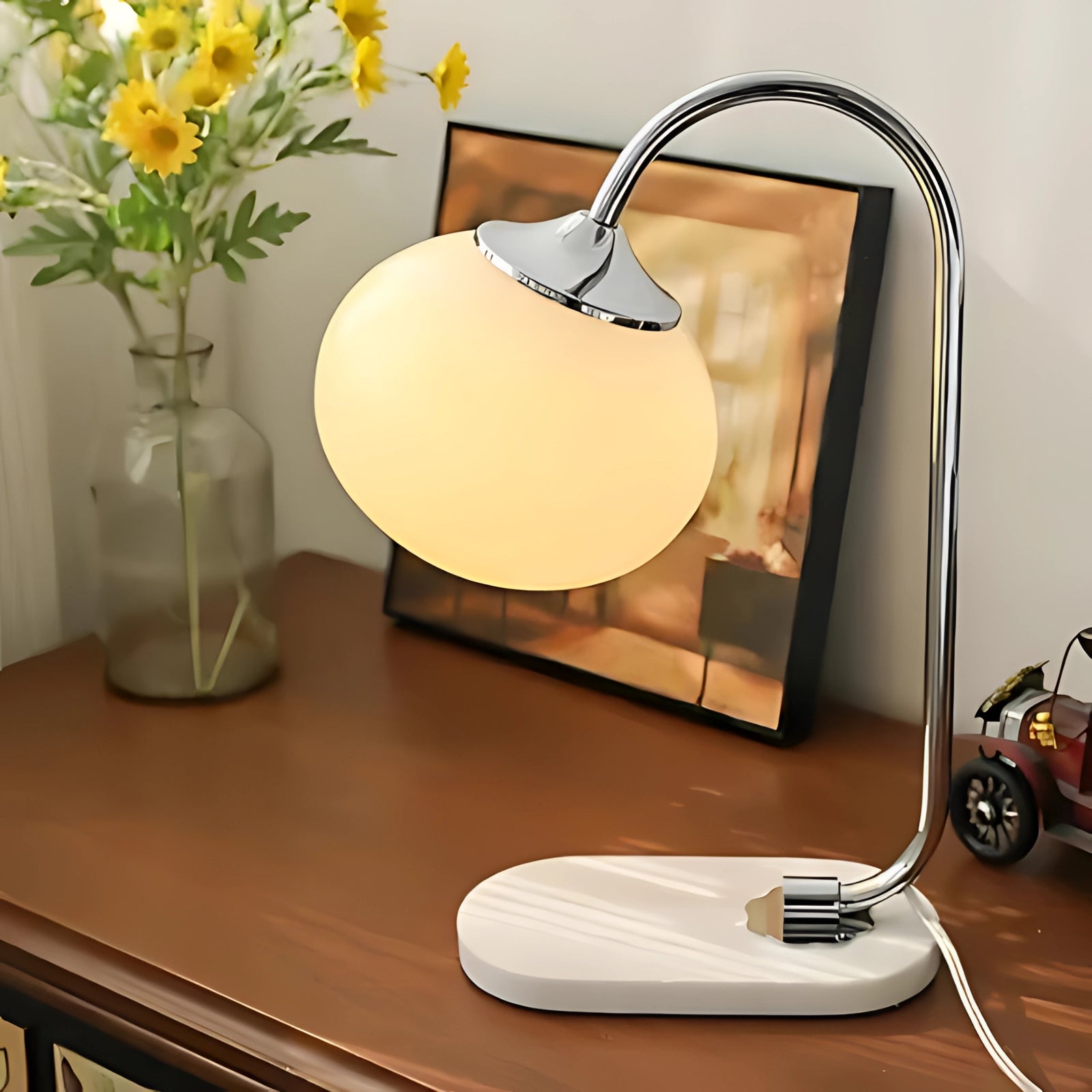 Modern gold finish table lamp with a minimalist curved design, featuring a silver and yellow color scheme, positioned beside a white flowerpot with a green houseplant on a tabletop.