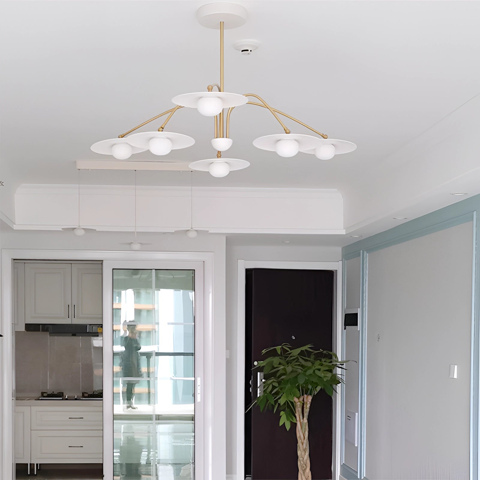 Modern mid-century chandelier with a gold finish and opal glass shades, elegantly hanging in a stylish interior setting. The room features wooden elements, houseplants, and natural light streaming through a window, creating a warm and inviting ambiance.