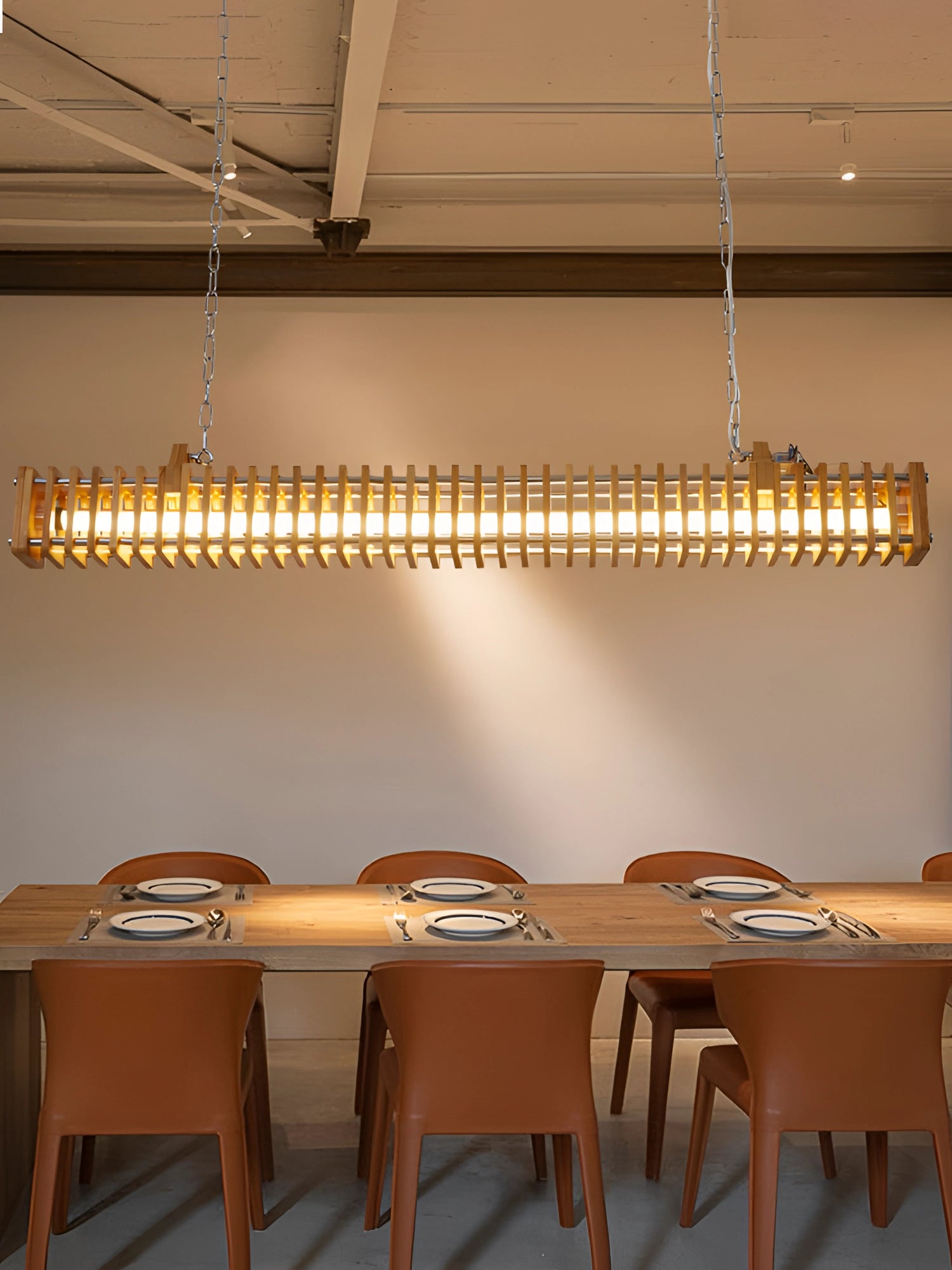 Modern gold linear pendant light chandelier with adjustable chain hanging above a wooden table and chairs, enhancing the interior design of the room with its elegant lighting.