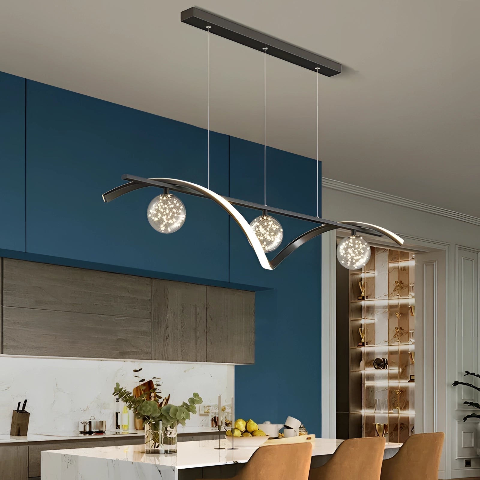 Modern gold pendant light chandelier hanging above a contemporary dining room setting featuring a wooden table, surrounded by stylish furniture and houseplants, enhancing the interior design with a luxurious touch.