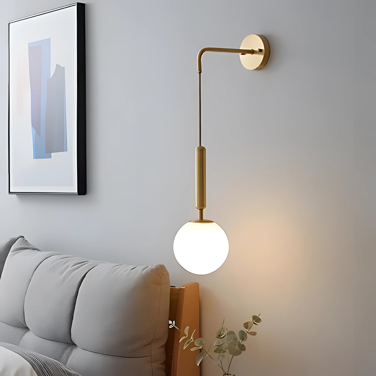 Modern gold wall lamp with adjustable LED sconce in a brass finish, mounted on a light-colored wall. The lamp is positioned above a couch with wooden elements, contributing to a comfortable interior design. A picture frame is visible nearby, enhancing the stylish and warm ambiance.