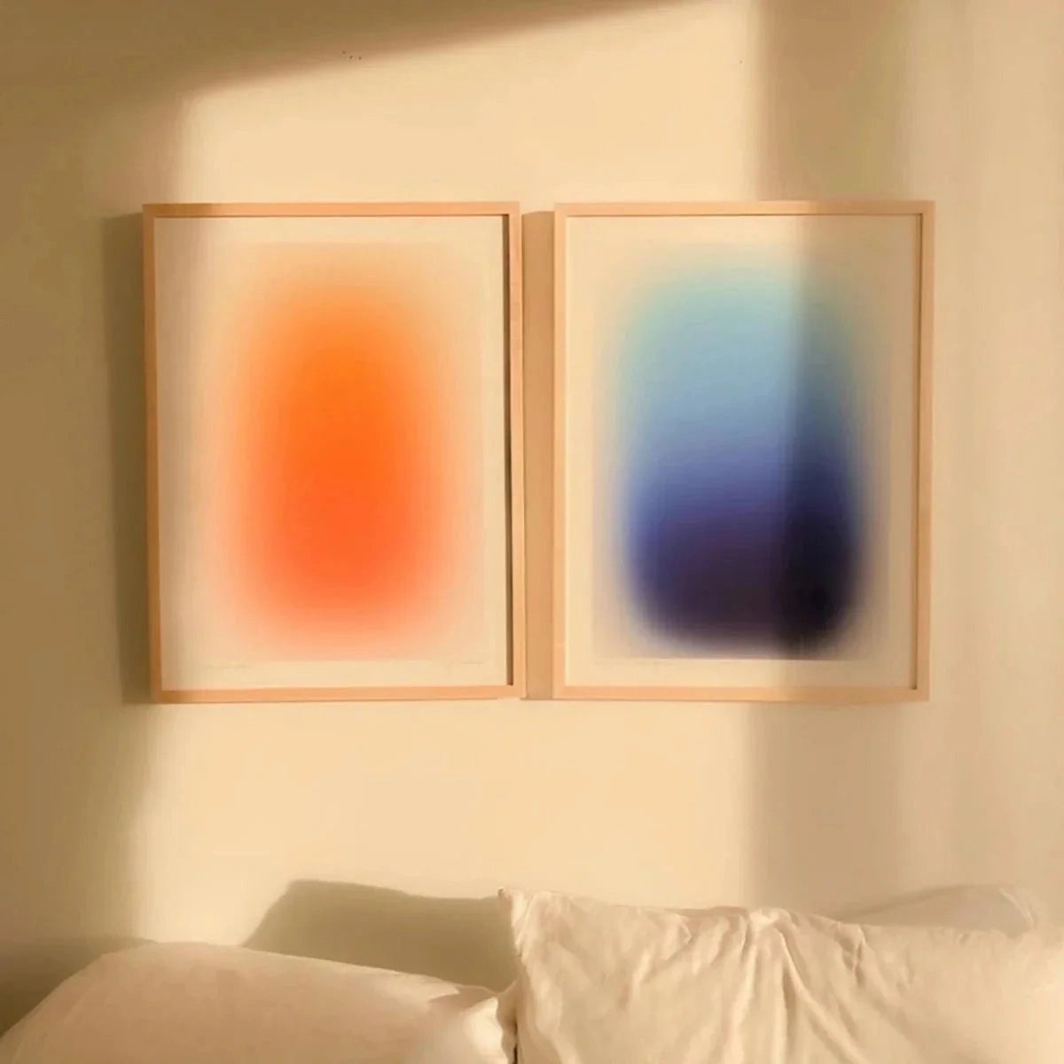 Modern gradient wall art featuring a blend of orange and blue hues on a rectangular canvas, displayed above a couch with a wooden picture frame, enhancing the minimalist decor of the interior space.