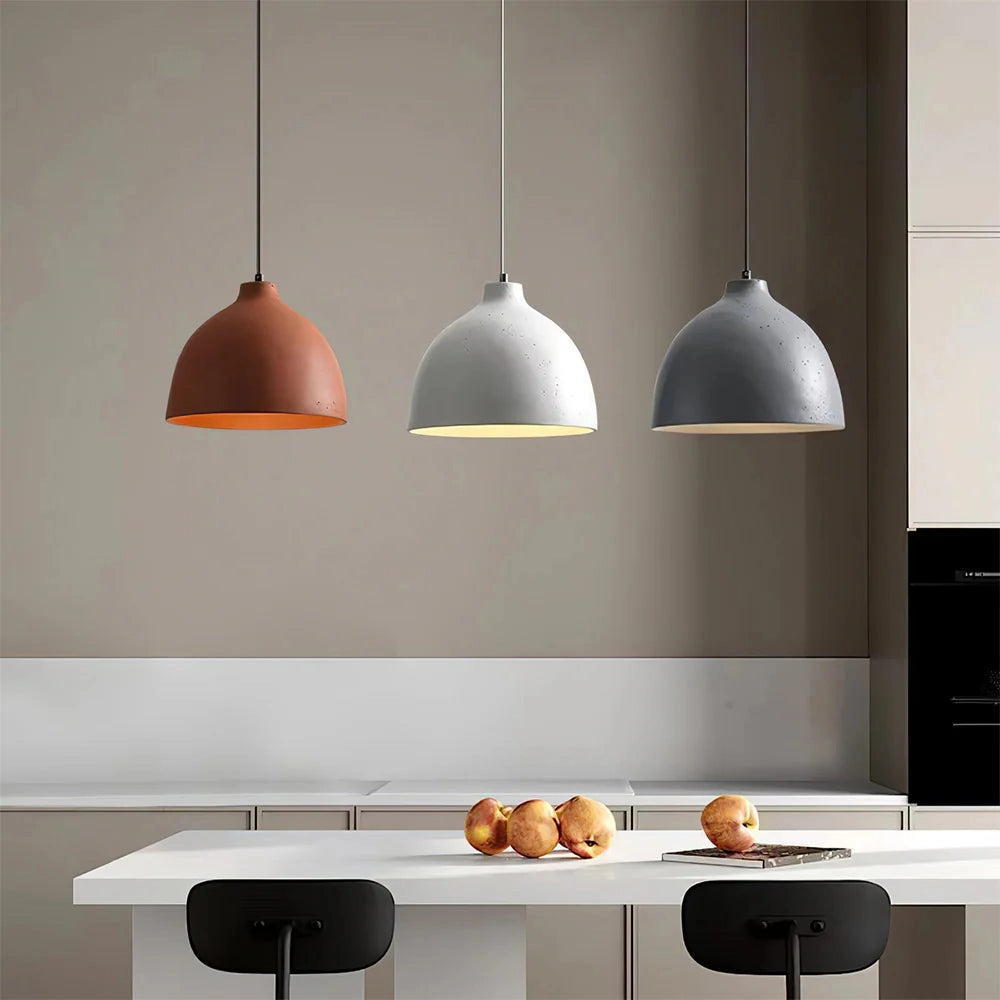 Modern industrial concrete pendant light with Scandinavian yellow accent hanging above a kitchen space featuring white and grey interiors, wooden shelving, and food items.