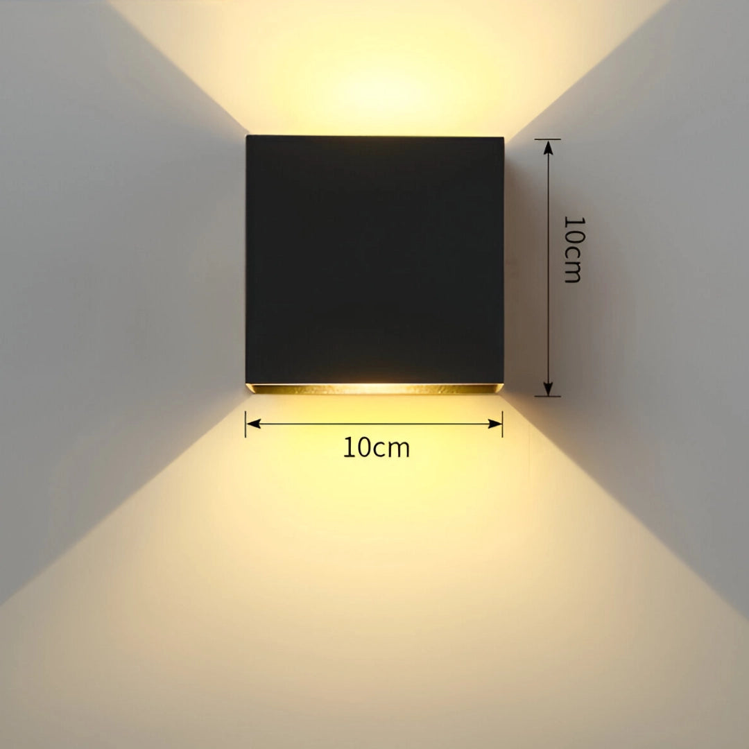 Modern white LED cube wall sconce mounted on the exterior wooden wall of a house, emitting cold white light against a clear sky backdrop.