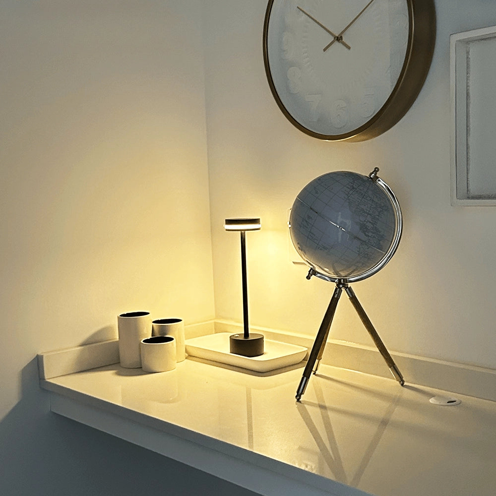 Modern black metal LED desk lamp with adjustable arm positioned on a wooden desk alongside a circular clock and picture frame, highlighting its sleek and energy-efficient design.