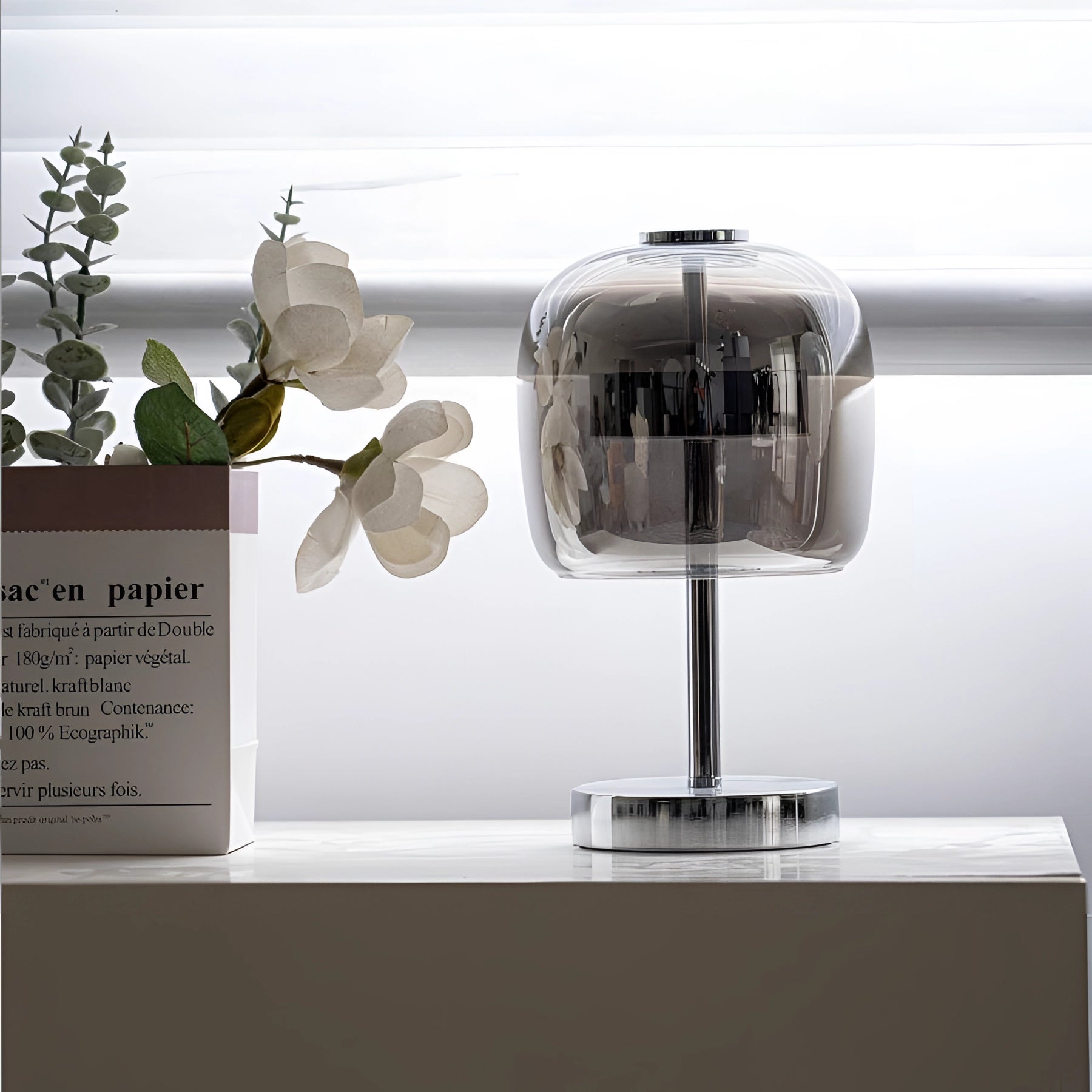 Modern LED glass lamp with a chrome base and transparent shade placed on a wooden shelf.