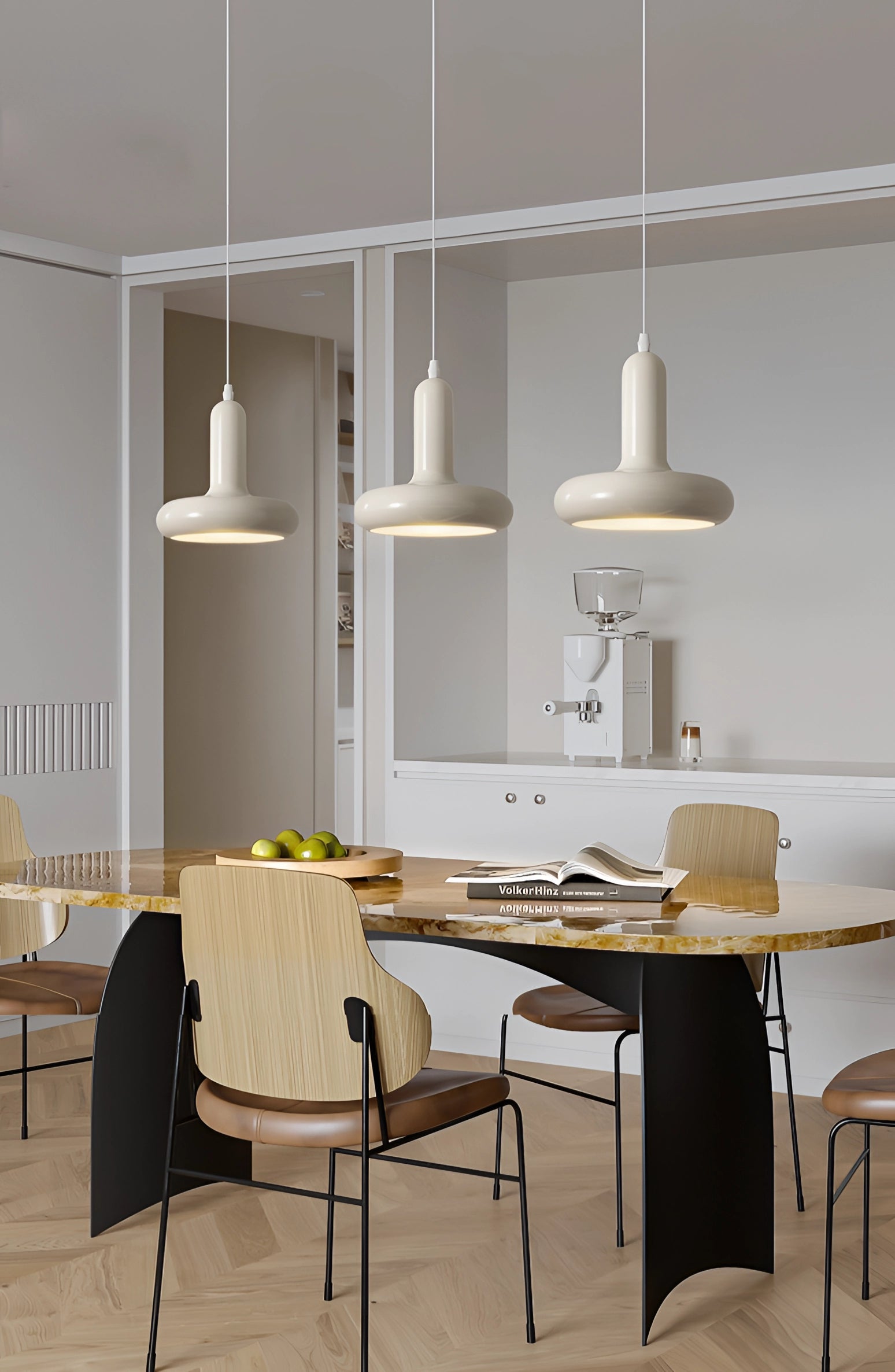 Modern LED pendant light hanging above a minimalist Scandinavian-style kitchen and dining area, featuring a wooden table, white chairs, and grey shelving against a white wall with a smooth floor.