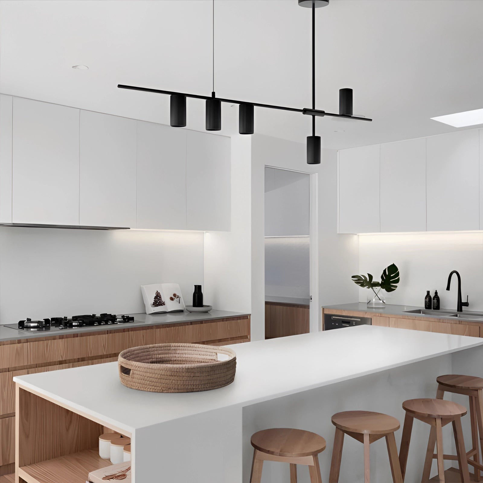 Modern LED pendant light in matte black, hanging above a wooden kitchen table, with contemporary interior design elements and shelving in the background.